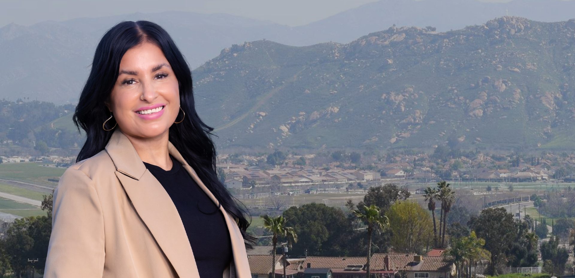 Adriana Gonzalez smiling in a tan blazer, with the hills and homes of Jurupa Valley behind her